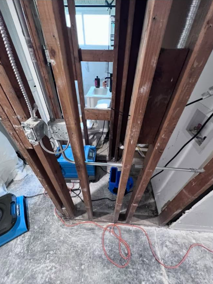 Exposed wall studs with dehumidifier and air movers running behind a bathroom